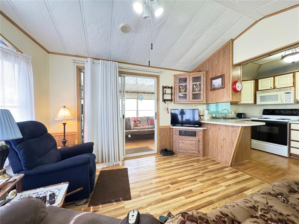 A living room with wood-look flooring, a blue recliner, and an open kitchen with wood cabinets — 4900 BRITNI WAY Lot 70, ZEPHYRHILLS, FL