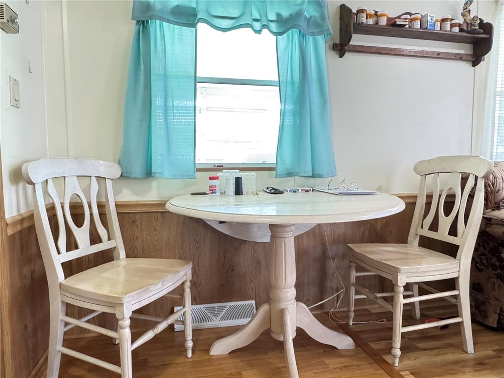 A small dining area features a round white table, two wooden chairs, and blue curtains — 4900 BRITNI WAY Lot 70, ZEPHYRHILLS, FL