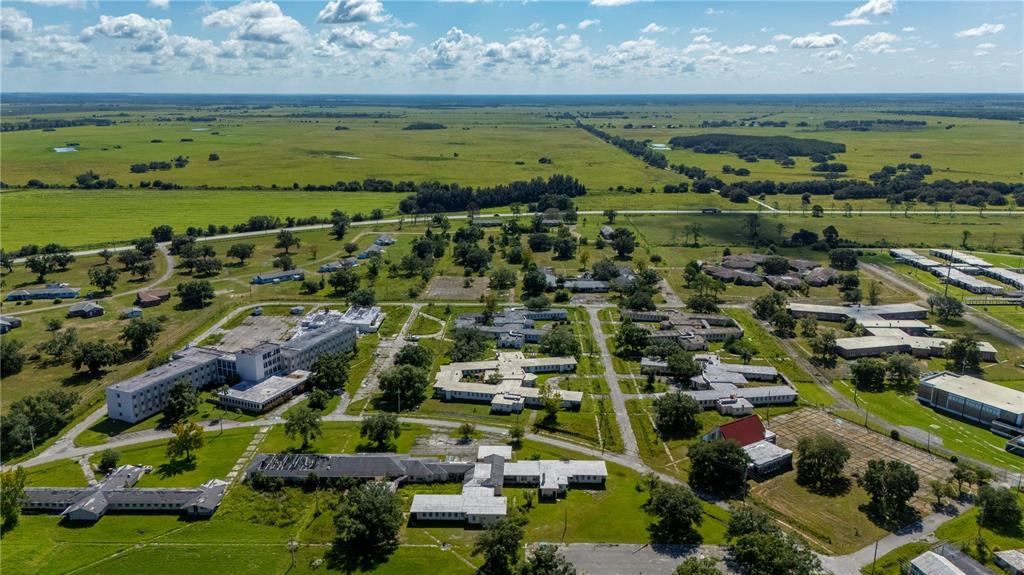 An aerial view shows a large, abandoned complex of buildings surrounded by expansive green fields — 6000 SE HWY 31, ARCADIA, FL