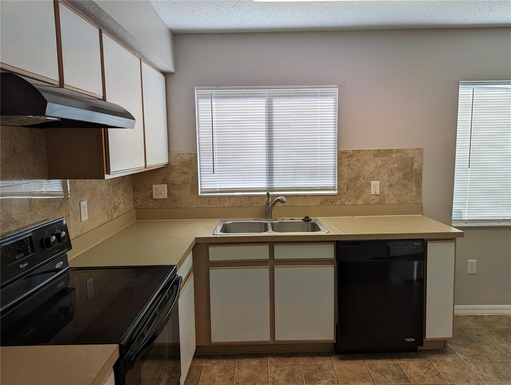 A kitchen features white cabinets, tan countertops, a black dishwasher, and a black stove — 3120 SUMMER HOUSE DRIVE, VALRICO, FL