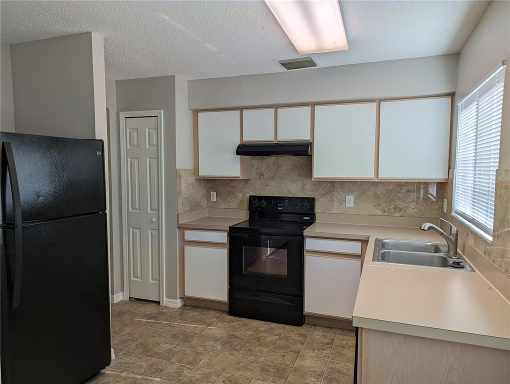 A kitchen with black appliances, white cabinets, tan countertops, and a tiled backsplash — 3120 SUMMER HOUSE DRIVE, VALRICO, FL