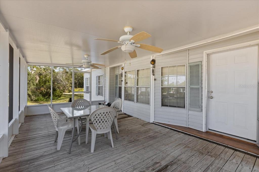 A covered wooden deck features a dining set, two ceiling fans, and a white door — 4945 SW 358 HIGHWAY, STEINHATCHEE, FL