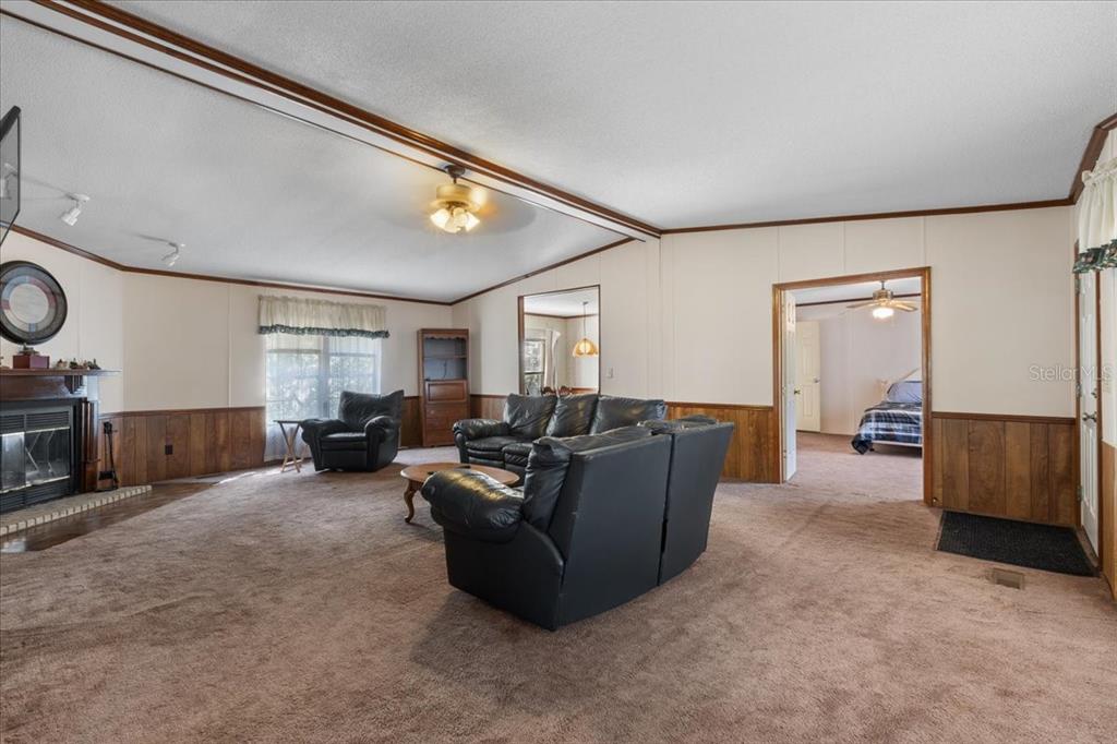 A living room features brown carpeting, wood wainscoting, a fireplace, and black leather furniture — 4945 SW 358 HIGHWAY, STEINHATCHEE, FL