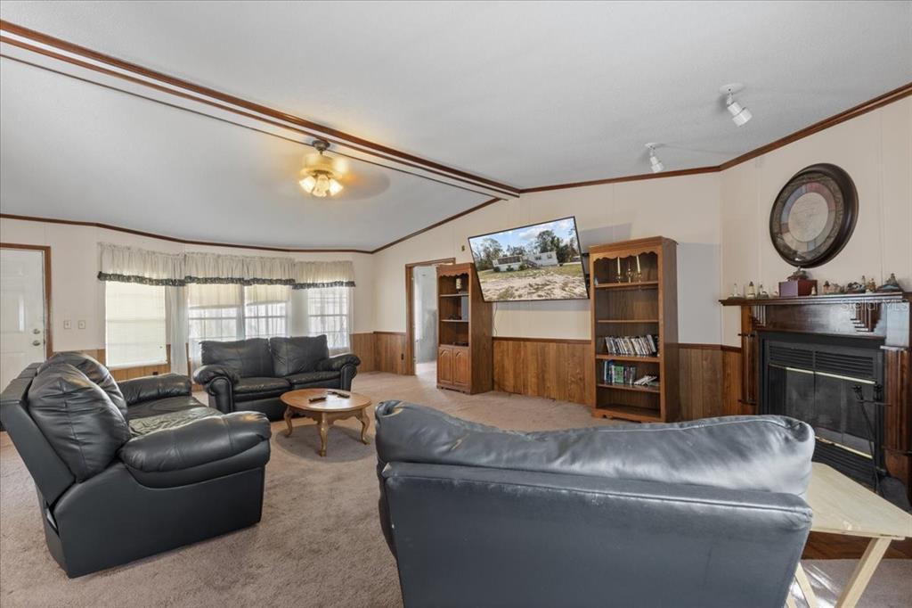 A living room features a fireplace, wood paneling, black leather furniture, and a wall-mounted television — 4945 SW 358 HIGHWAY, STEINHATCHEE, FL