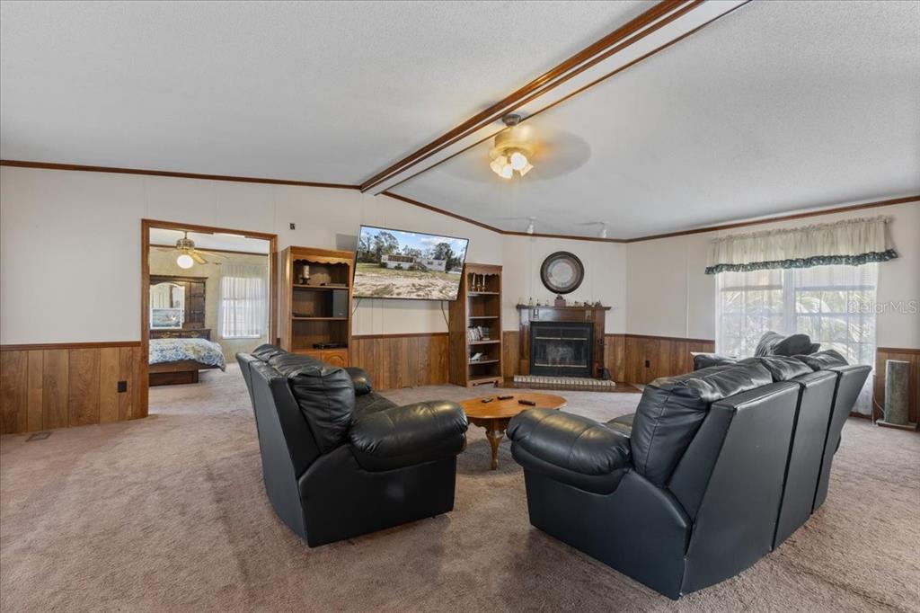 A living room features brown carpeting, wood paneling, a fireplace, and two black leather sofas — 4945 SW 358 HIGHWAY, STEINHATCHEE, FL