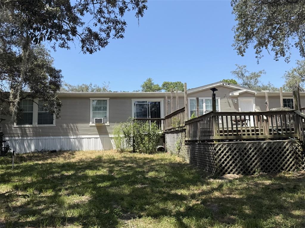 The exterior of a single-story manufactured home features light siding and a large wooden deck — 12091 PINETREE LANE, BROOKSVILLE, FL