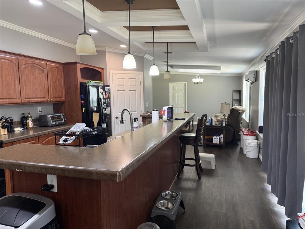 A kitchen with wood cabinets, a long breakfast bar, and pendant lighting opens to a living area — 12091 PINETREE LANE, BROOKSVILLE, FL