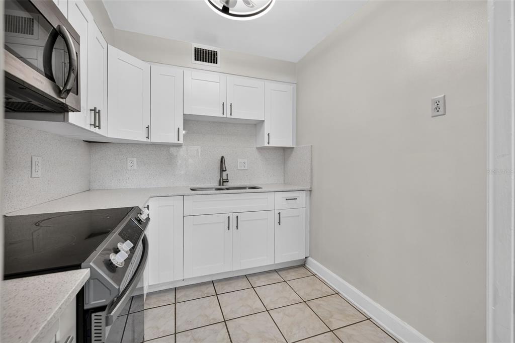A small kitchen features white cabinets, a stainless steel microwave, a stove, and tiled floors — 1000 79TH AVENUE N UNIT 111, ST PETERSBURG, FL