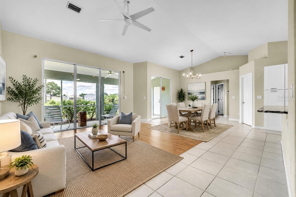 An open-concept living and dining area with vaulted ceilings, tile flooring, and sliding glass doors — 485 BOUNDARY BOULEVARD, ROTONDA WEST, FL