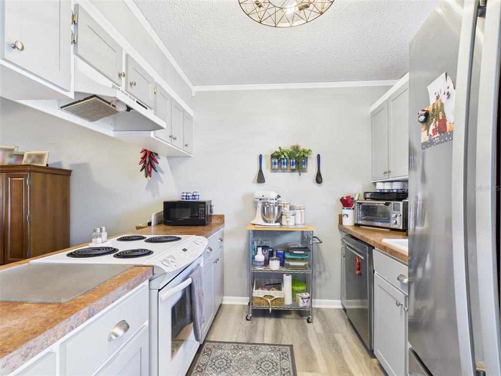 A galley kitchen features gray cabinets, laminate countertops, stainless steel appliances, and wood-look flooring — 4529 MERCADO DRIVE, SEBRING, FL