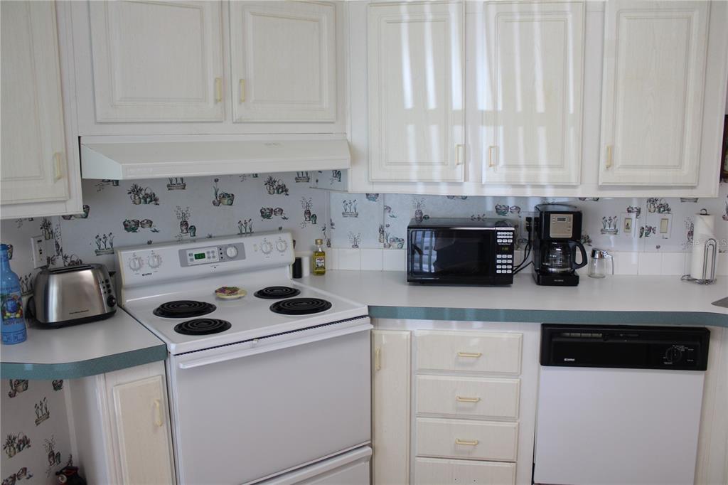 A kitchen features white cabinets, a white electric stove, a microwave, and patterned wallpaper — 8314 NANCY LANE, ELLENTON, FL