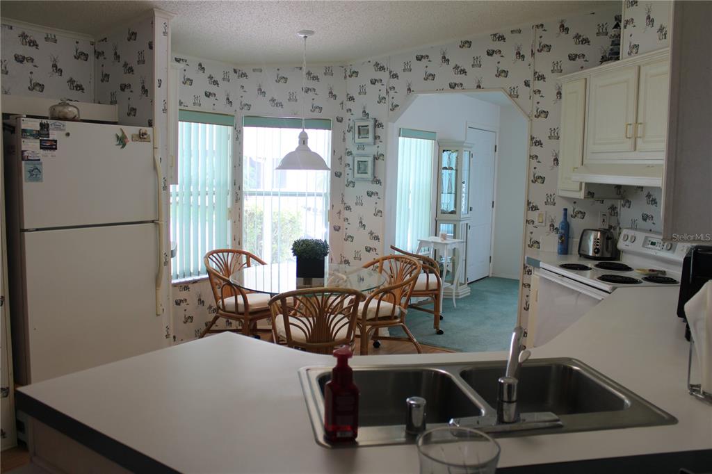A kitchen with white cabinets, a double sink, and a breakfast nook with patterned wallpaper — 8314 NANCY LANE, ELLENTON, FL