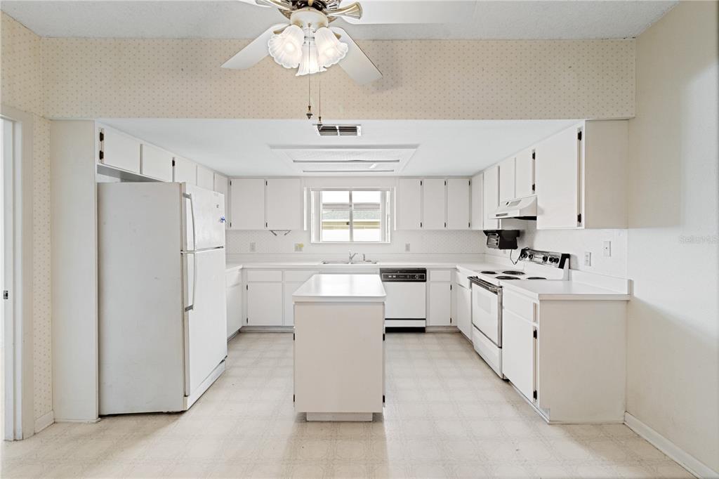 A white kitchen features a central island, white appliances, and cabinets under a ceiling fan — 3433 GLEN ABBEY LANE, LAKELAND, FL