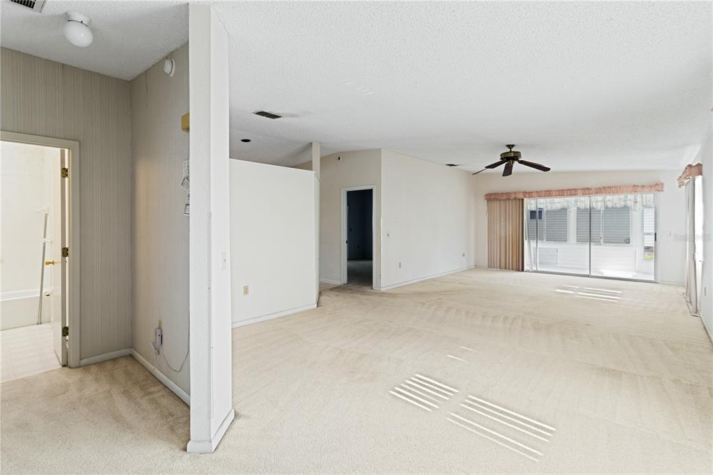 A carpeted living room features a ceiling fan, a sliding glass door, and an adjacent bathroom — 3433 GLEN ABBEY LANE, LAKELAND, FL