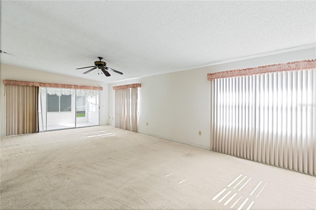 An empty living room with beige carpet, a ceiling fan, and large windows with vertical blinds — 3433 GLEN ABBEY LANE, LAKELAND, FL