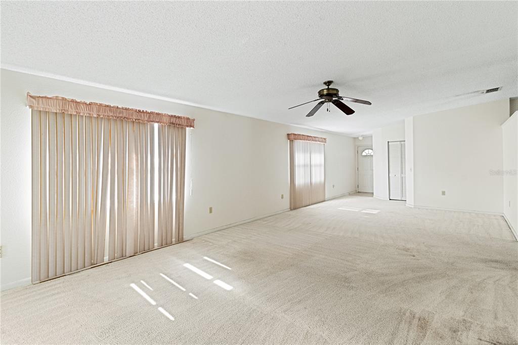 A spacious, carpeted living room features a ceiling fan, vertical blinds, and neutral wall paint — 3433 GLEN ABBEY LANE, LAKELAND, FL