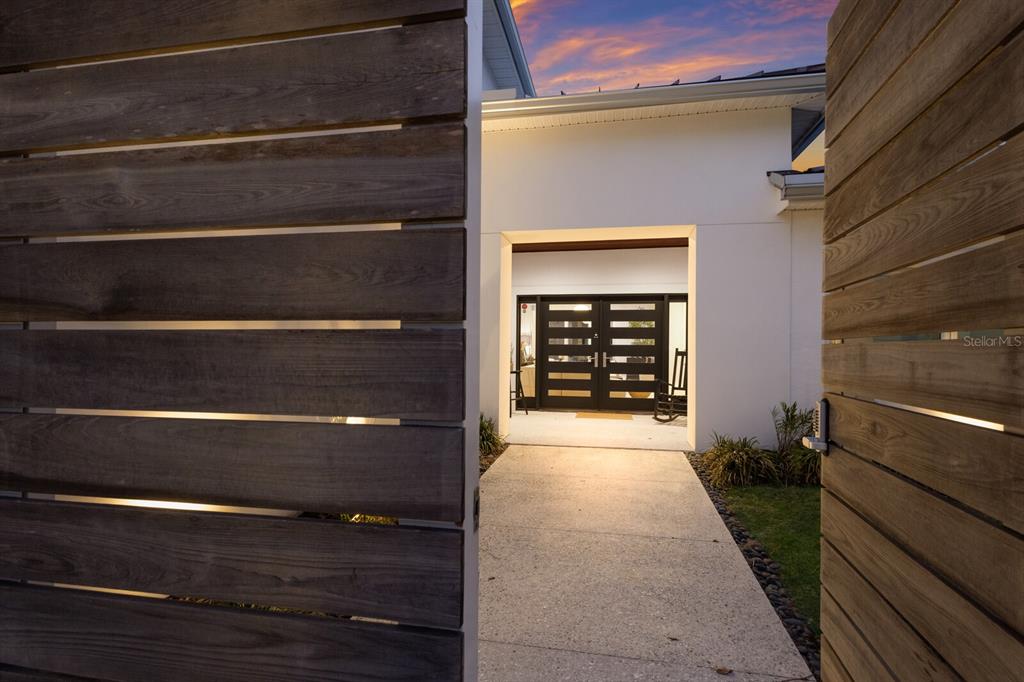 A concrete walkway leads through an open wooden gate toward a modern house entrance — 238 ISLAND CIRCLE, SARASOTA, FL