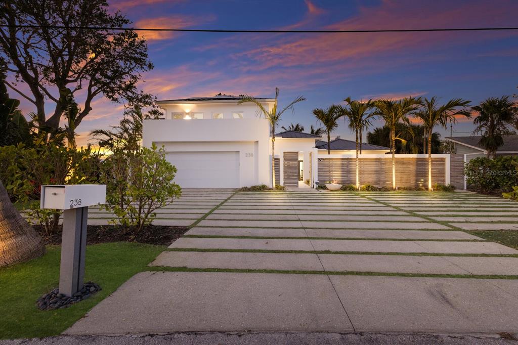 A modern white house with a paved driveway and palm trees at sunset — 238 ISLAND CIRCLE, SARASOTA, FL