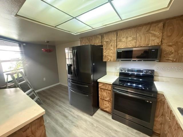 A kitchen features wood-grain cabinets, stainless steel appliances, and light-colored countertops under a drop ceiling — 2131 RIDGE ROAD S UNIT 74, LARGO, FL