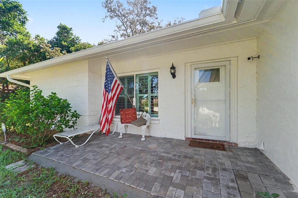A paved front porch features a white bench, an American flag, and a white door — 8521 CEDARVIEW COURT, PORT RICHEY, FL
