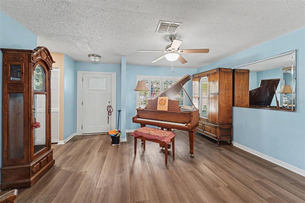 A living room features light blue walls, wood-look flooring, a grand piano, and a grandfather clock — 8521 CEDARVIEW COURT, PORT RICHEY, FL
