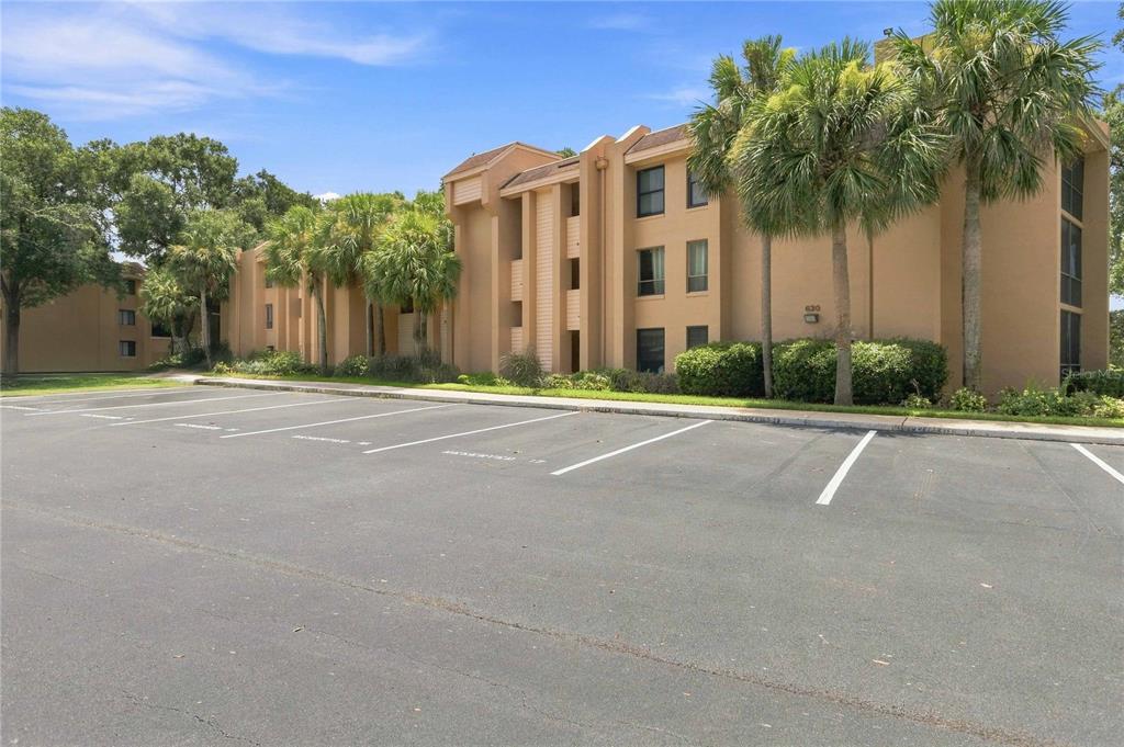 A multi-story tan apartment building stands behind a paved parking lot with palm trees — 620 CRANES WAY UNIT 303, ALTAMONTE SPRINGS, FL