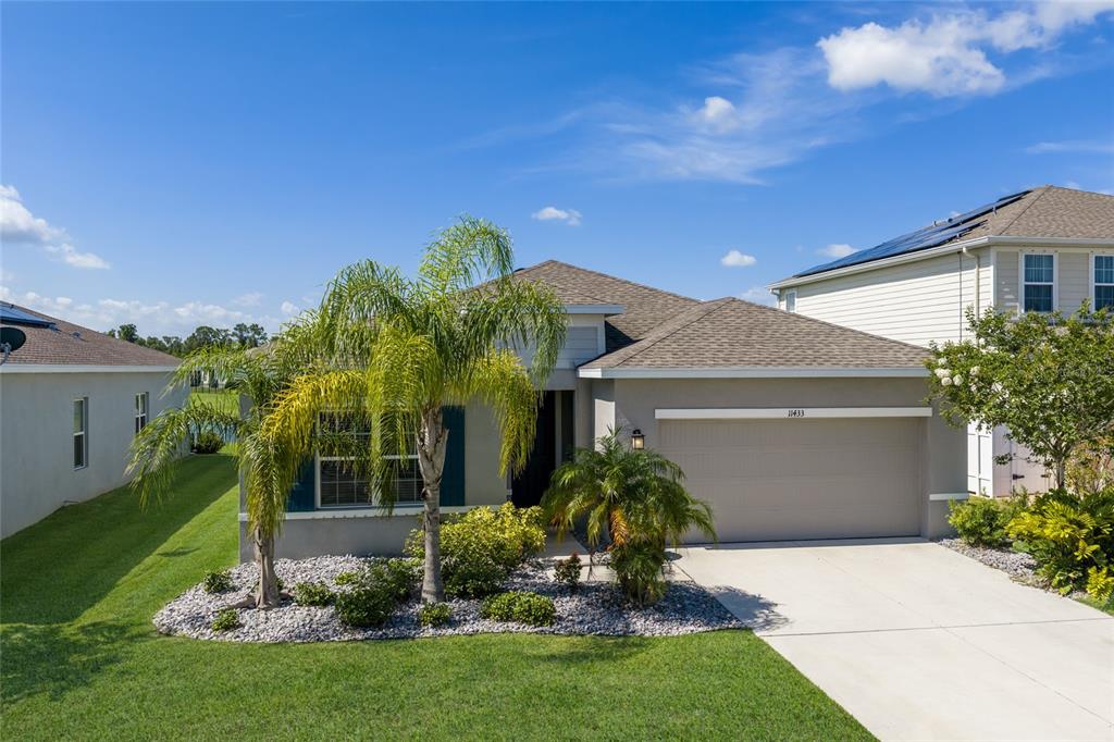 A single-story house with a two-car garage, palm trees, and a gravel landscaping bed — 11433 64TH STREET E, PARRISH, FL