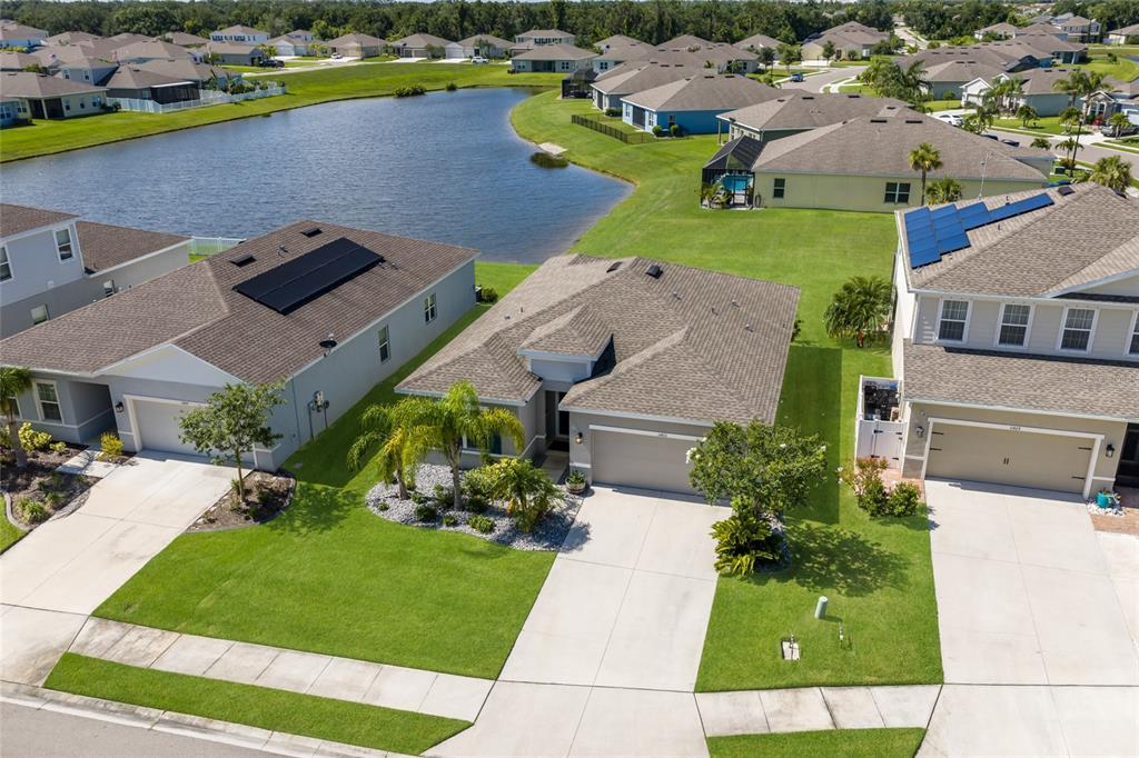 An aerial view shows three suburban houses with driveways and lawns near a small lake — 11433 64TH STREET E, PARRISH, FL