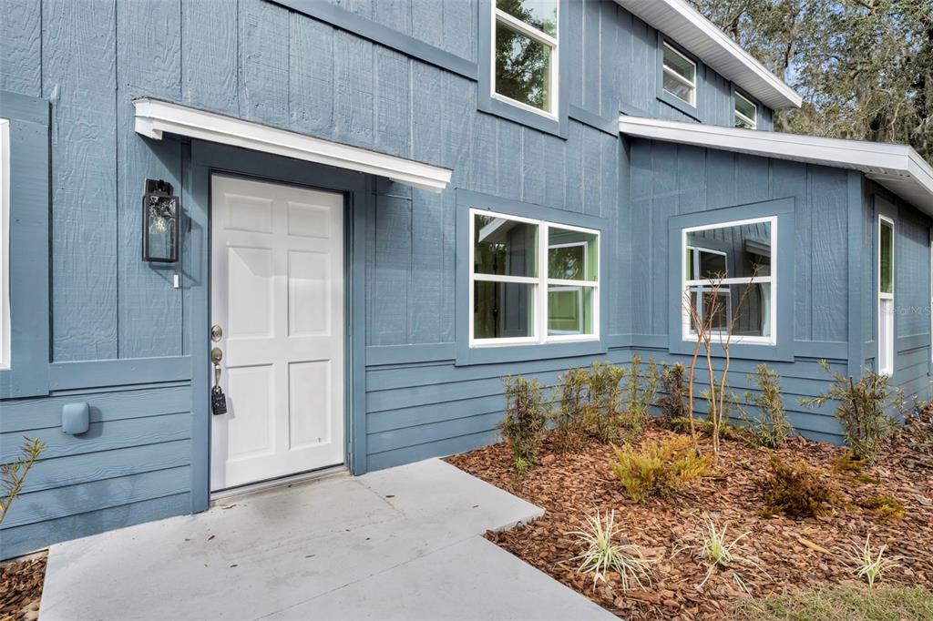 A blue house exterior features a white front door, a small awning, and landscaping — 31201 MERRY RD, TAVARES, FL