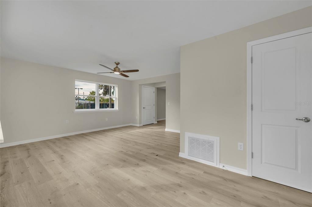 An empty room features light wood-look flooring, beige walls, a ceiling fan, and white doors — 31201 MERRY RD, TAVARES, FL