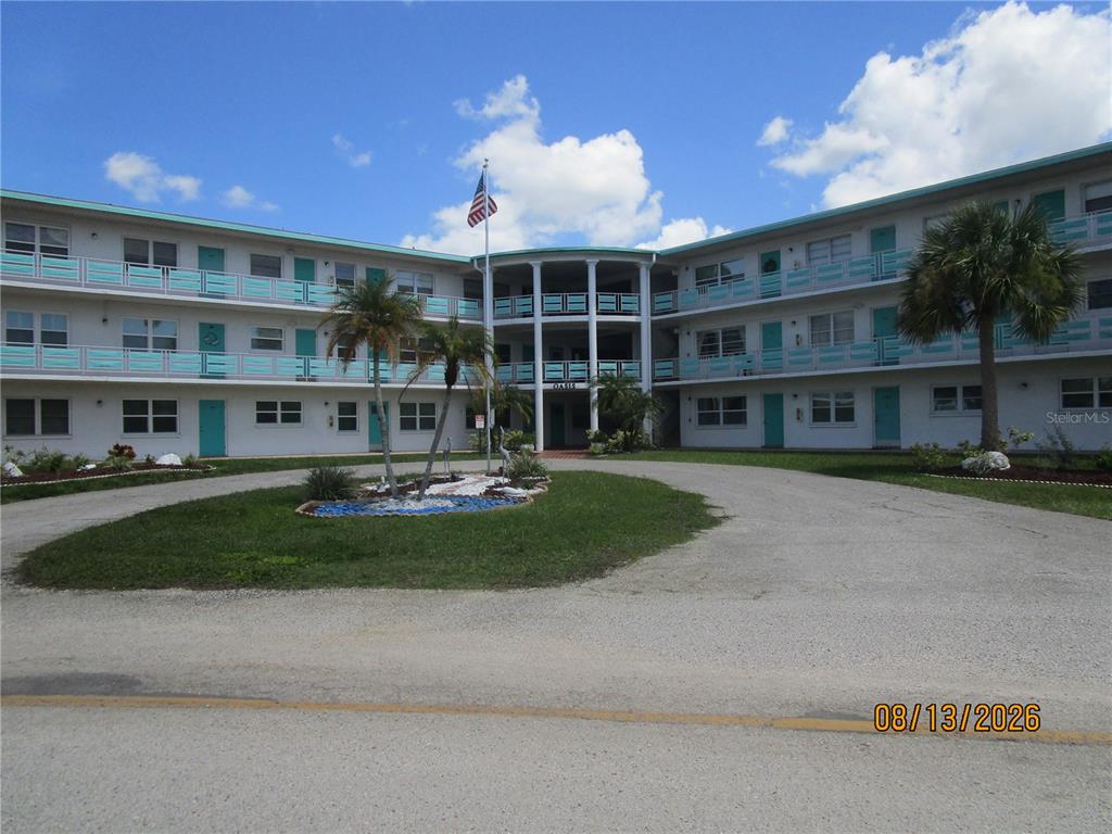 A three-story apartment building with a circular driveway and palm trees in the foreground — 1900 59TH AVENUE N UNIT 115, ST PETERSBURG, FL