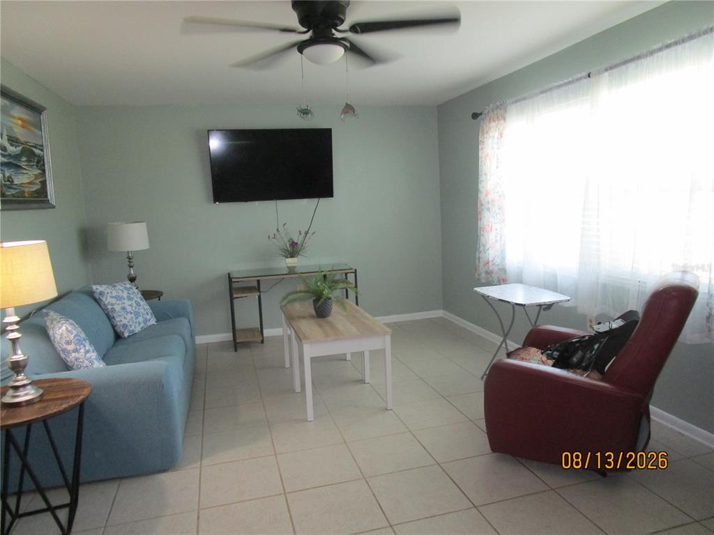 A living room features a blue sofa, a red recliner, a television, and tile flooring — 1900 59TH AVENUE N UNIT 115, ST PETERSBURG, FL