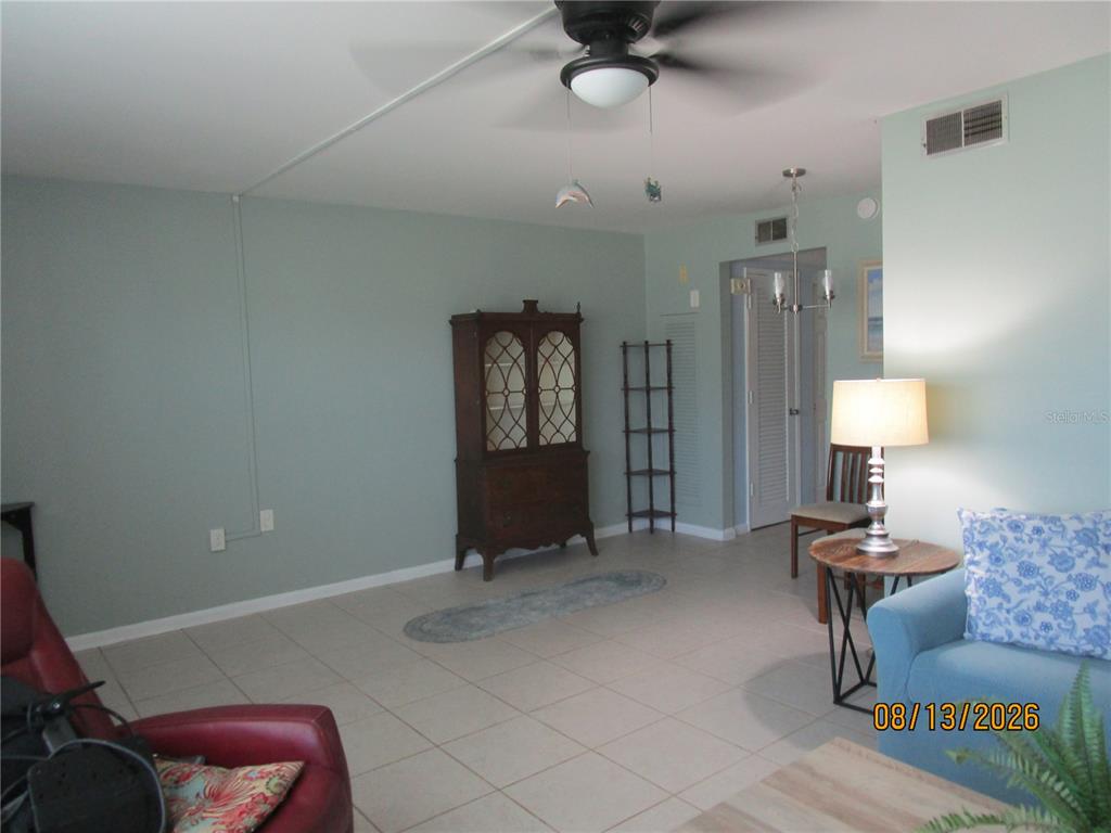 A living room features light green walls, tile flooring, a ceiling fan, and wooden furniture — 1900 59TH AVENUE N UNIT 115, ST PETERSBURG, FL