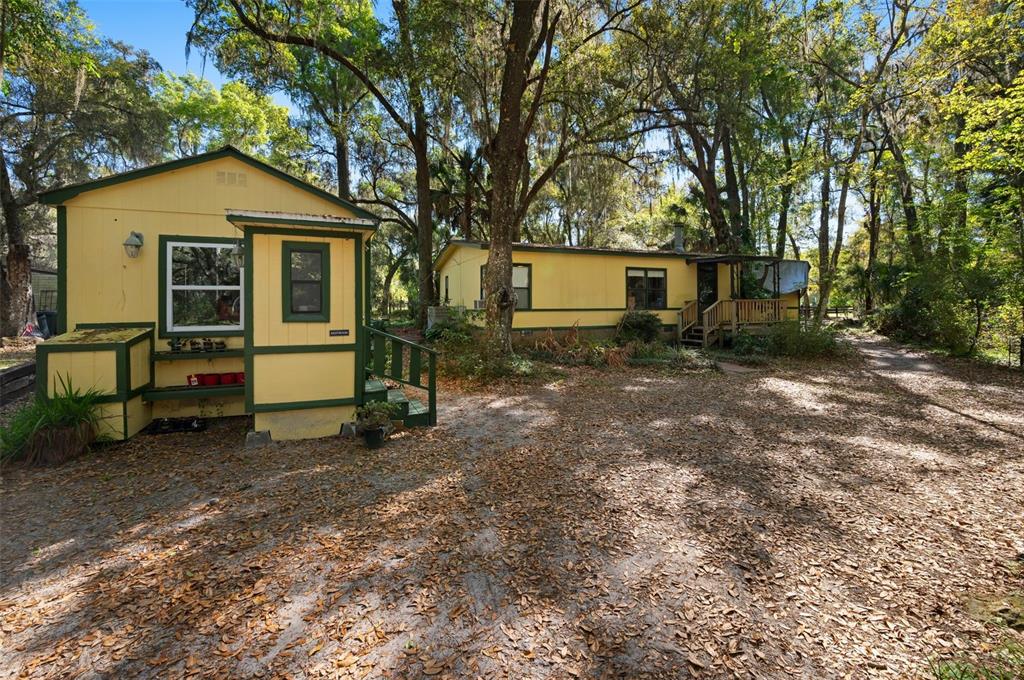 A dirt path leads through a wooden fence toward a small shed under large trees — 15311 SW 107TH STREET, ARCHER, FL
