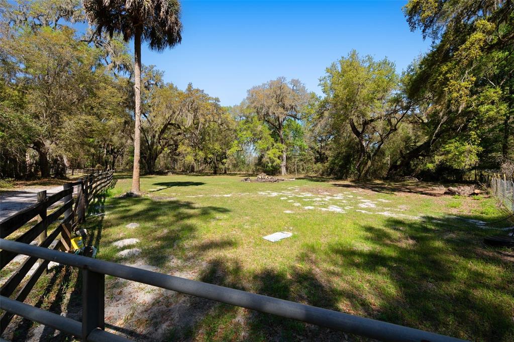 A fenced grassy lot features scattered rocks and mature trees under a clear blue sky — 15311 SW 107TH STREET, ARCHER, FL
