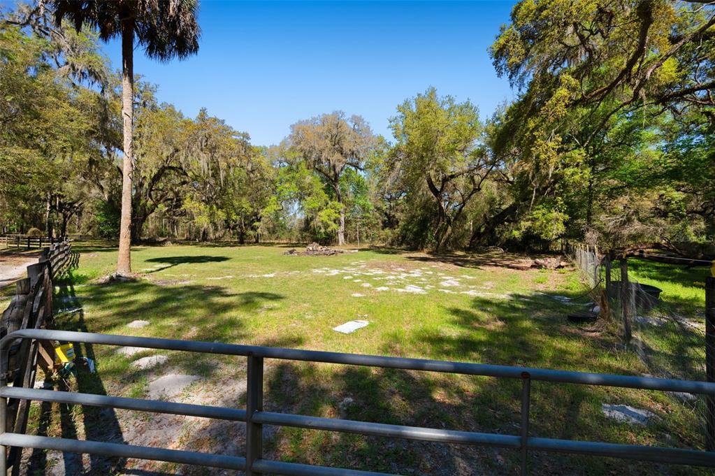 A dirt path leads through a metal gate into a wooded area with large trees — 15311 SW 107TH STREET, ARCHER, FL
