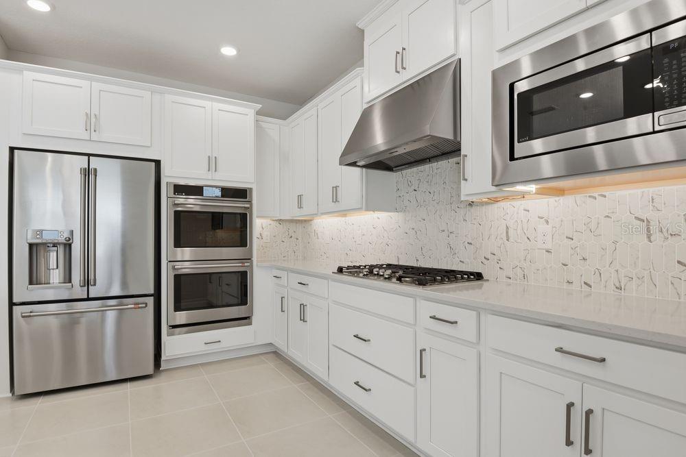A modern kitchen features white cabinetry, stainless steel appliances, and a marble-patterned tile backsplash — 664 JUNONIA BOULEVARD, NEW SMYRNA BEACH, FL