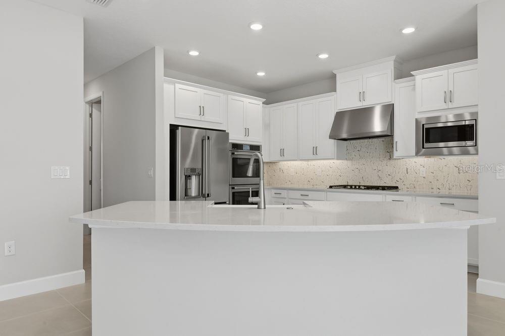A modern kitchen features white cabinetry, a large island, stainless steel appliances, and quartz countertops — 664 JUNONIA BOULEVARD, NEW SMYRNA BEACH, FL