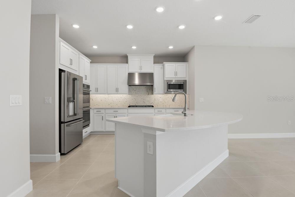 A modern kitchen features white cabinetry, stainless steel appliances, and a large quartz-topped island — 664 JUNONIA BOULEVARD, NEW SMYRNA BEACH, FL