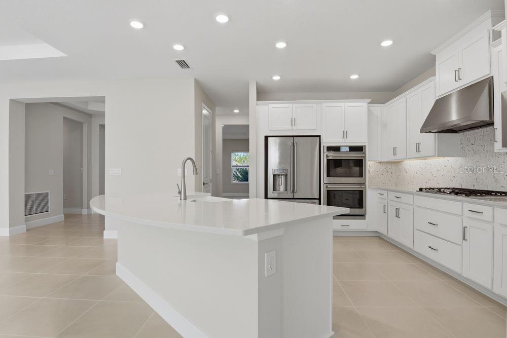 A modern kitchen features white cabinetry, a large quartz island, and stainless steel appliances — 664 JUNONIA BOULEVARD, NEW SMYRNA BEACH, FL