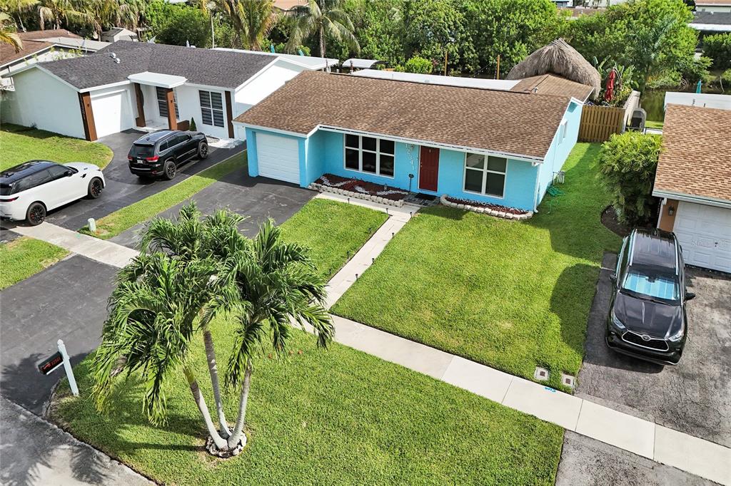 An aerial view shows three suburban houses with driveways, lawns, and a canal in back — 12341 NW 29TH MANOR, SUNRISE, FL