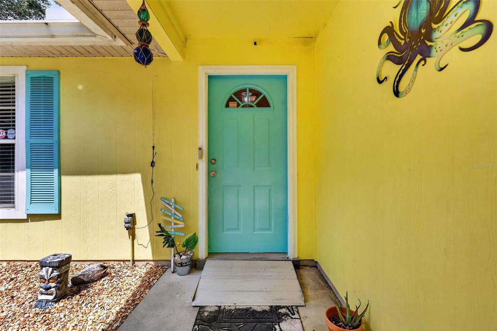 A bright yellow house exterior features a turquoise front door and a decorative octopus wall hanging — 39627 GREENBRIER STREET, EUSTIS, FL