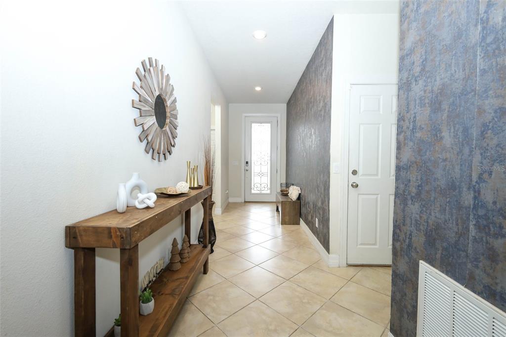 A bright entryway features a wooden console table, tile flooring, and a textured accent wall — 2190 BUR OAK BLVD, ST CLOUD, FL