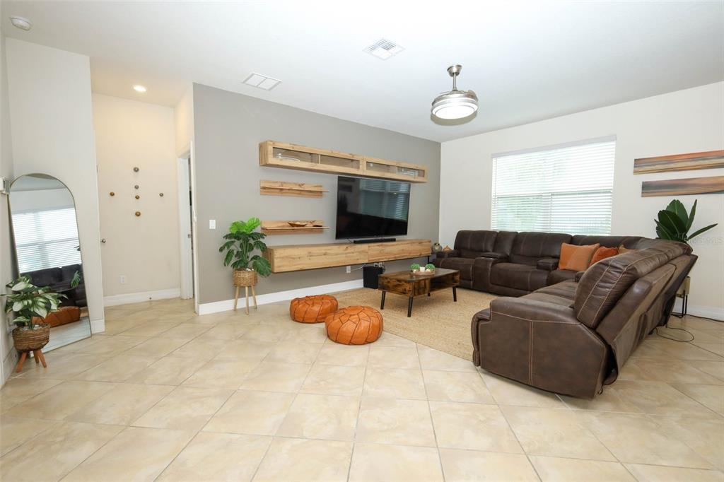 A living room features a brown sectional sofa, a wall-mounted media console, and tile flooring — 2190 BUR OAK BLVD, ST CLOUD, FL
