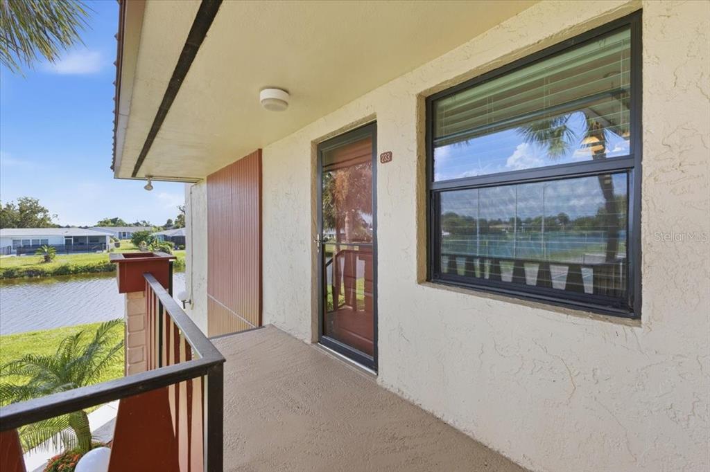 An exterior balcony with a metal railing overlooks a canal and a tennis court — 66 BOUNDARY BOULEVARD UNIT 233, ROTONDA WEST, FL
