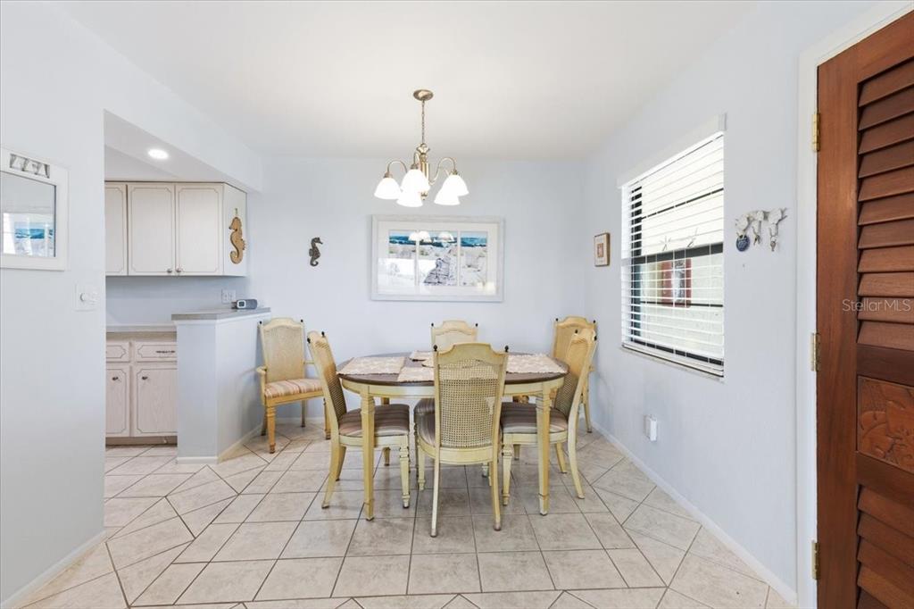 A dining room features a round table with six chairs, tile flooring, and a chandelier — 66 BOUNDARY BOULEVARD UNIT 233, ROTONDA WEST, FL