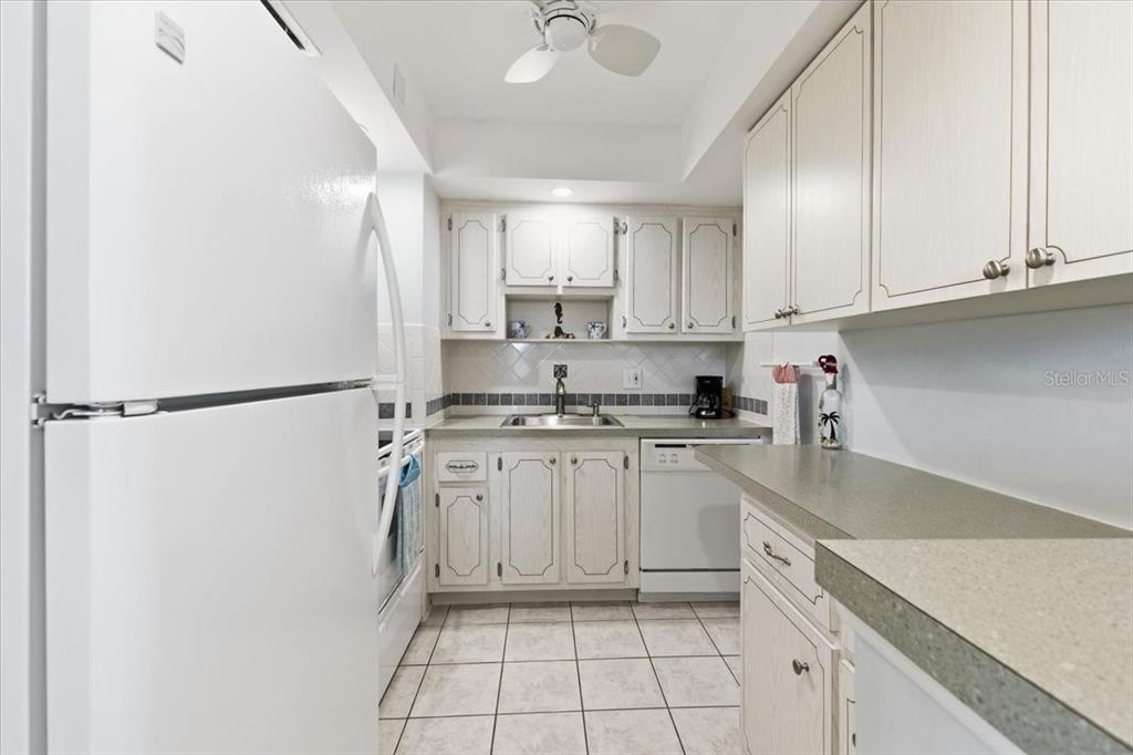 A galley kitchen features white cabinets, light-colored countertops, a tiled floor, and white appliances — 66 BOUNDARY BOULEVARD UNIT 233, ROTONDA WEST, FL