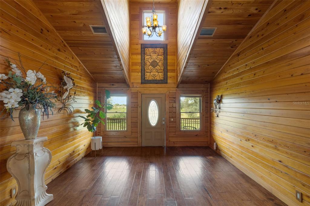 A high-ceilinged entryway features wood-paneled walls, dark flooring, a chandelier, and a front door — 39730 CARLTON ROAD, PARRISH, FL