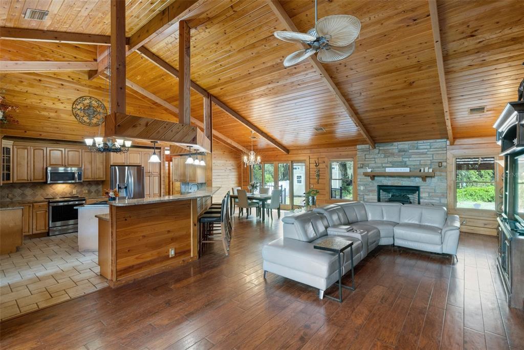 An open-concept living room and kitchen with wood-paneled vaulted ceilings and a stone fireplace — 39730 CARLTON ROAD, PARRISH, FL