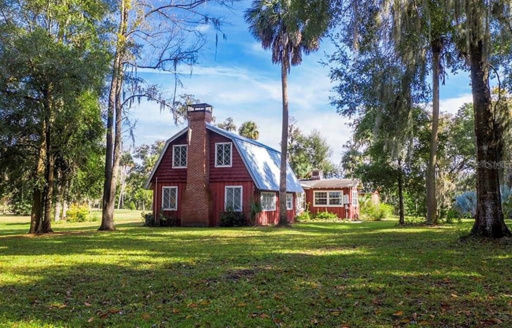 A red barn-style house with a brick chimney stands in a grassy, tree-filled yard — 327 TANGLEWILDE STREET, APOPKA, FL